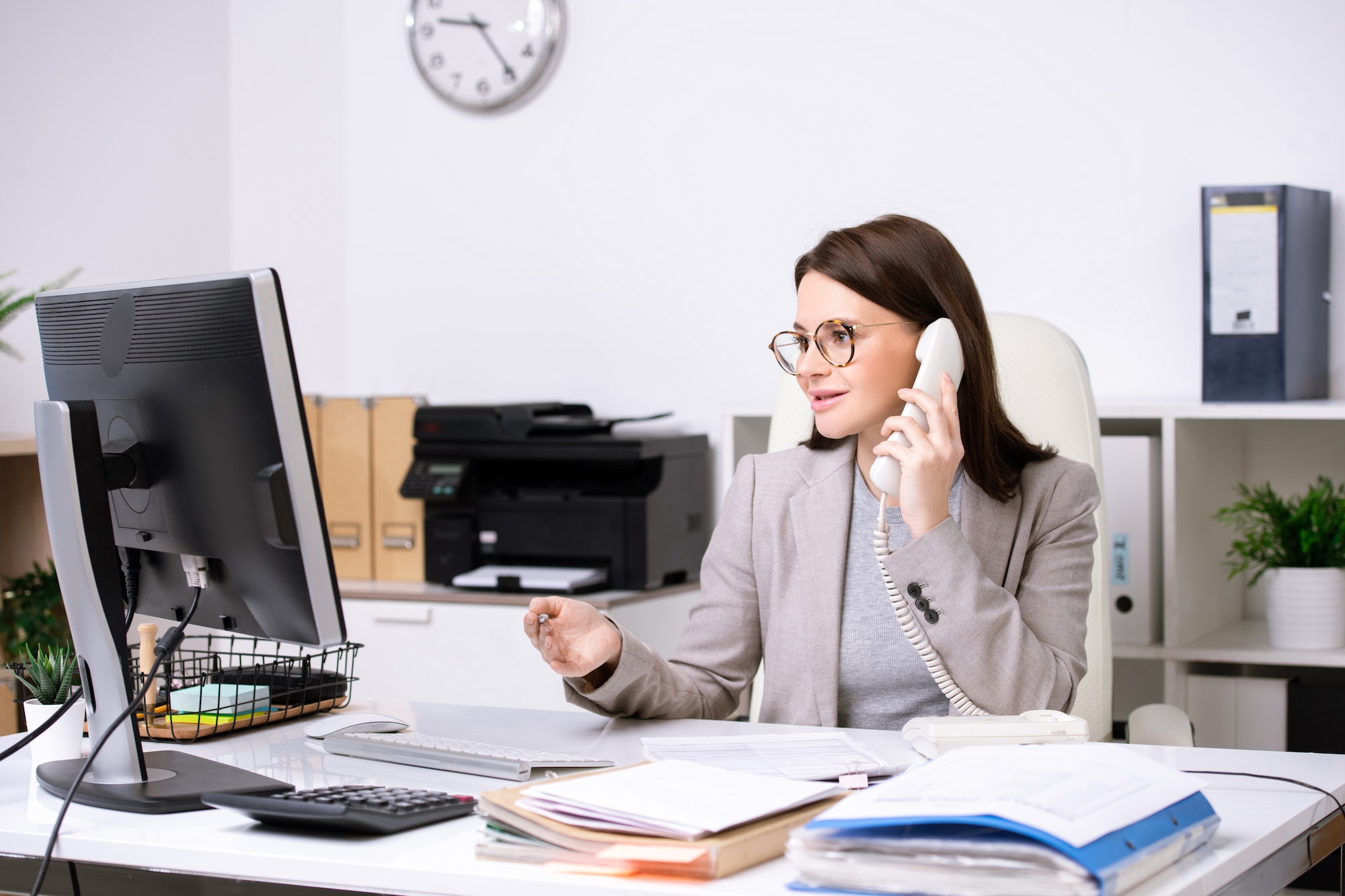 Pretty young secretary working by desk in front of computer monitor